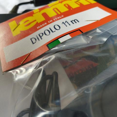 étiquette cartonnée colorée (rouge; écriture jaune "lemm"; encart blanc "dipolo 11m"; drapeau italien). accrochée à une pochette plastique. un fil noir torsadé est visible dedans.