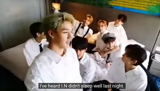 Bang Chan films a video of skz hanging out in a hotel room. Felix has his arm around I.N's neck. Caption: I've heard I.N didn't sleep well last night