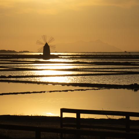 Mulino a vento in siloutte al tramonto sulle saline di trapani col riflesso sull'acqua