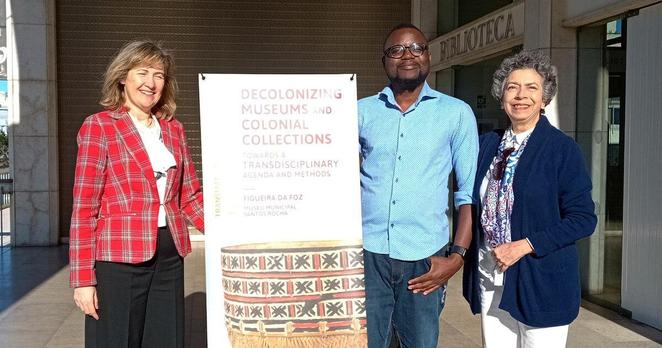 Photo of Elisabete Pereira, Robert Nyamushosho, Marília Xavier Cury, and the banner of the conference "Decolonizing Museums and Colonial Collections. Towards a Transdisciplinary Agenda and Methods" at the entrance of the Santos Rocha Municipal Museum.