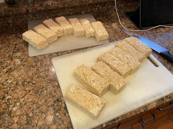 14 rectangular pieces of rice-and-marshmallow confections arranged on two plastic cutting boards.