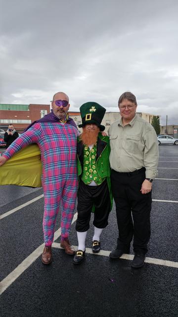Three men posing in costumes, the middle one dressed as a leprechaun.