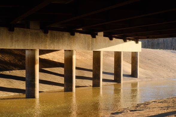 Underneath an overpass, concrete columns taper away as the golden hour sun rise causes halation on the structure’s surfaces