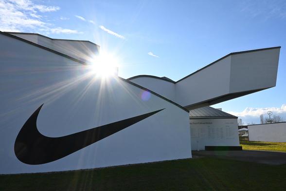 a side wall of the vitra design museum by frank gehry, there is a large black Nike Swoosh painted on the white wall, about 10m long. Sun shines towards camera over the roof, with some lens flare.
