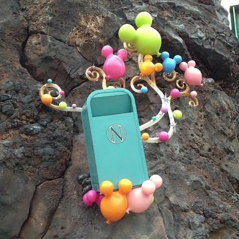 Artwork installed on a rock formation featuring a green trash cans and many balloons in the shape of Mickey Mouse heads