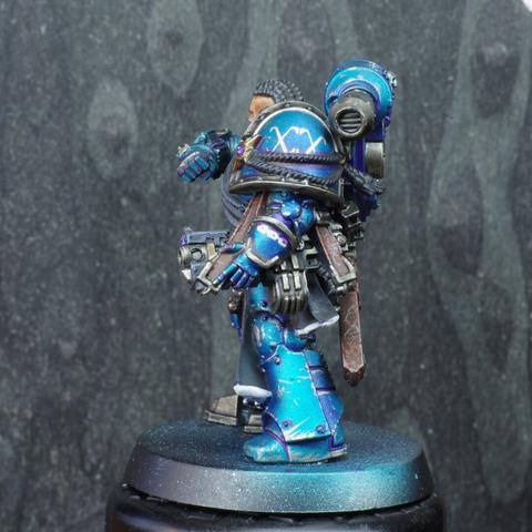 Left side of the mini, showing the bolter hooked by a leather strap. They have the 20 written in roman numerals on their shoulder pad. A chain symbol is present on their vambrace