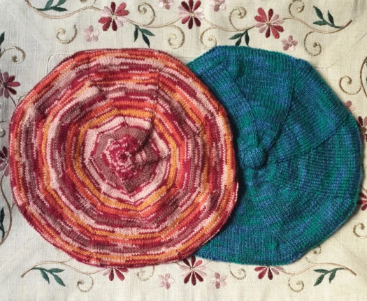 Deux bérets, l'un rouge-orange-rose, l'autre bleu et vert sur un fond décoré de rameau en broderie mécanique.