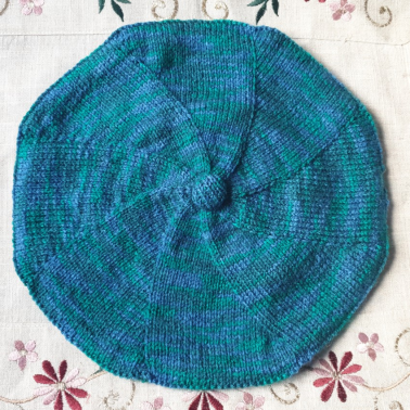 Béret vert et bleu lévogyre avec, en son centre, un gros bouton décoratif.
