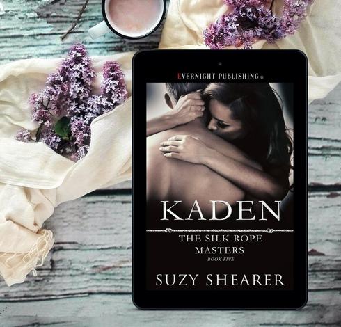 Ebook of Kaden by Suzy Shearer. Background is looking down on a lime-washed wooden surface with a cream scarf casually laid across.  There are bunches of mauve & white small flowers resting on the scarf. Above the scarf is a cup of cocoa.