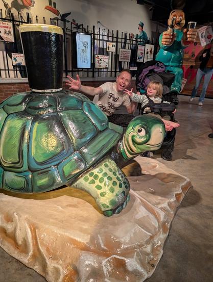 Patrick and his son Patrick gesturing toward a statue of a turtle holding a glass of Guinness.