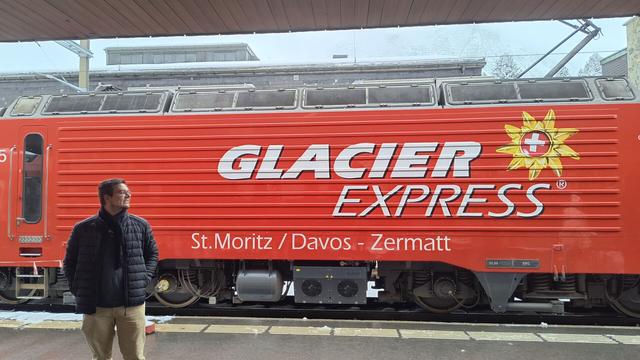 I am standing in front of a red loco HGe 4/4 II number 105 which belongs to the Matterhorn-Gotthardt railway. In the loco it reads "Glacier Express: St. Moritz / Davos - Zermatt".