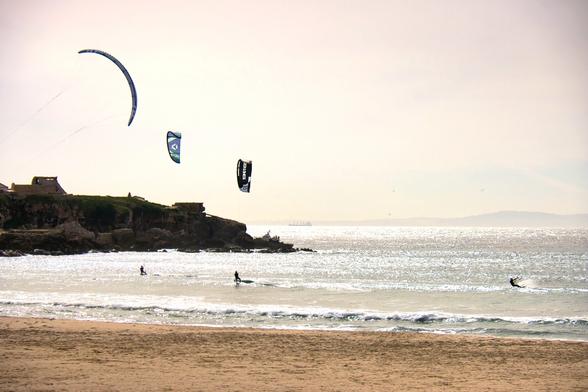 tre persone che fanno kitersurf in una spiaggia, con le loro vele nel cielo.