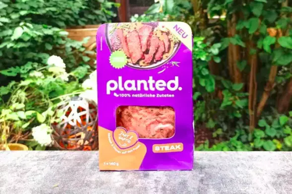 auf einem tisch vor grünem hintergrun steht eine lila packung der marke "planted" mit einem steak.