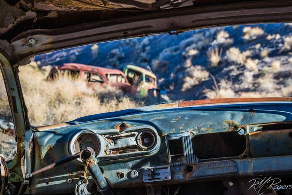 Photograph taken from inside of an old abandoned car in Death Valley thru the missing windshield at other old rusting vehicles.