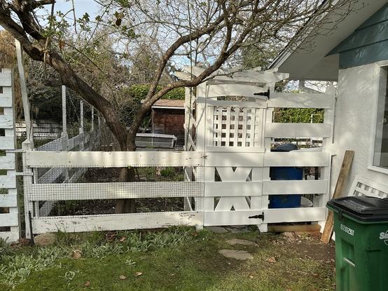 A white horizontal boarded fence being rebuilt.  Green trash can beside.