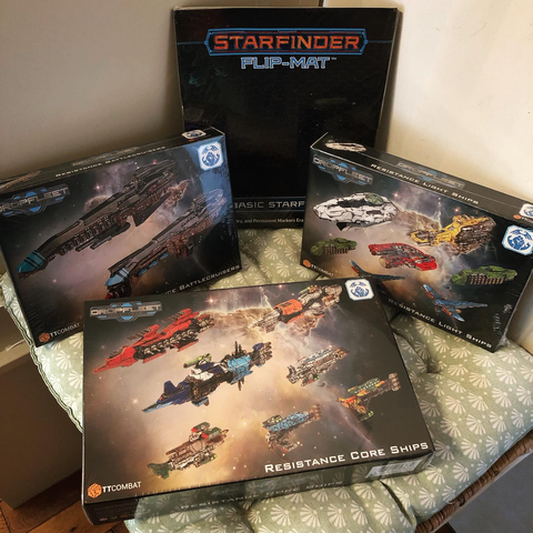 Plusieurs boites de vaisseaux (figurines à peindre) du jeu Dropfleet Commander, et plan de bataille spatiale de la gamme Starfinder.
