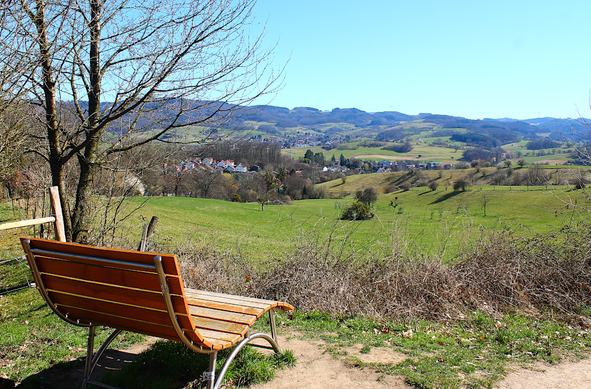 Liegebank mit Blick auf eine hügelige Landschaft mit Dörfern, Wiesen und Wäldern