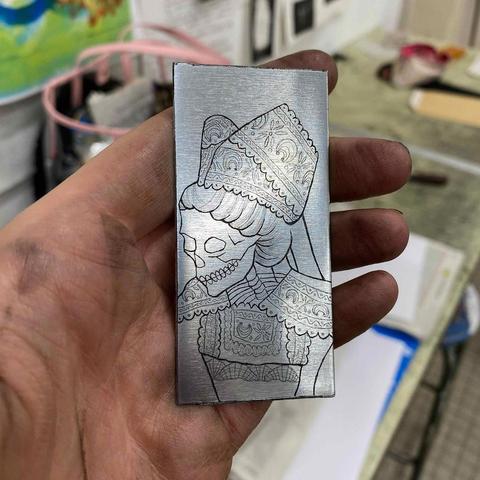 Plaque de zinc gravée représentant un squelette habillé d’un costume traditionnel Fouesnant, dont la coiffe et la collerette présentent de la dentelle aux motifs d’inspiration bigoudène.