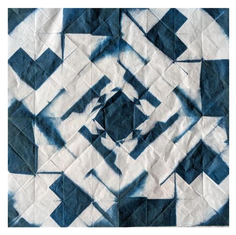 A piece of white paper which shows creases from being folded into an origami form - in this case a 'square dance kusudama' - and exposed as a cyanotype. This means it has blue geometric patterns all over it - a central diamond, two layers of diagonal lines around that, then a ring of blocks, and triangles at the corners