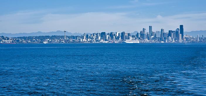 The Seattle skyline seen from a ferry in Elliott Bay. The water and sky are both different shades of blue which makes the buildings also appear blue