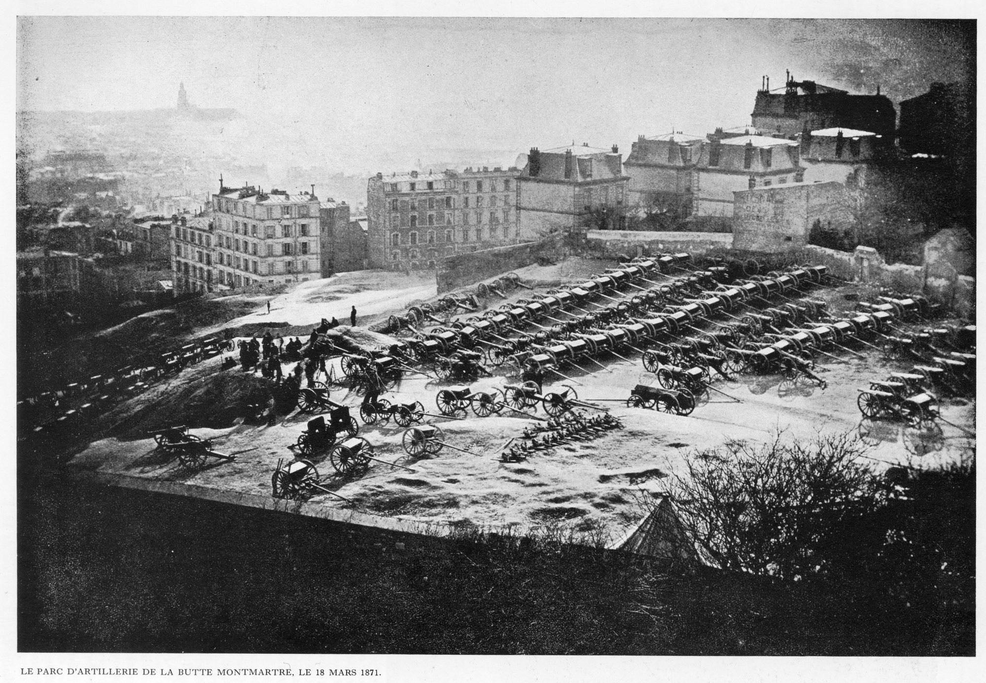 A photograph of the artillery park atop Montmartre on March 18, 1871. Cannons are set up in rows, with buildings in the background.