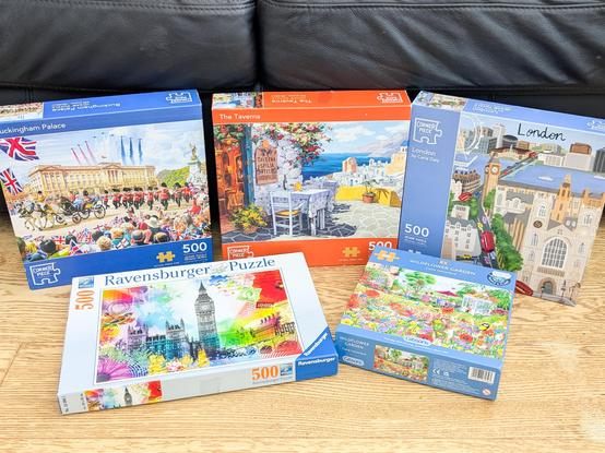 Five 500 piece jigsaw puzzle boxes arranged on a wooden floor.  There's a Greek taverna, a wildflower garden, and by sheer coincidence the other three are all London themed.