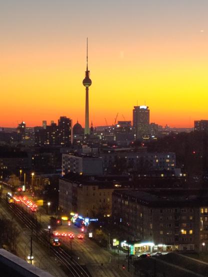 Der Berliner Fernsehturm vor rotgelbem Sonnenuntergang, aus erhöhter Perspektive aufgenommen. Etwas Stadt ist natürlich auch zu sehen.