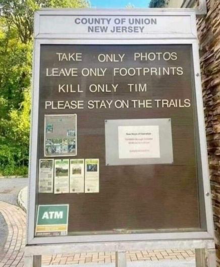 A park district sign for a hiking trail from "The County of Union New Jersey," with a glass cover and a tackboard inside. The tackboard has several paper flyers tacked on it, and the words "Take only photos... Leave only footprints... Kill only Tim. Please stay on the trails."

[The silent E is missing from "kill only time," so yes, it really does say "Tim."]