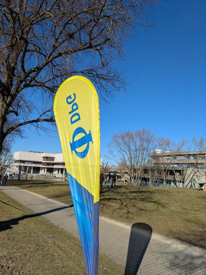 Windbanner der DPG in gelb-blauem Farbesign vor dem Hintergrund des Park-Campus' der Universität Regensburg