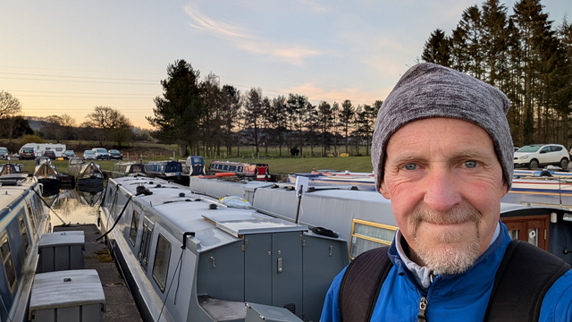 Selfie outside my narrowboat which is moored in a marina while I'm away travelling. It's a beautiful early spring morning, the sun is about to rise, and there's a frost on the ground and the narrowboat cabin roof.