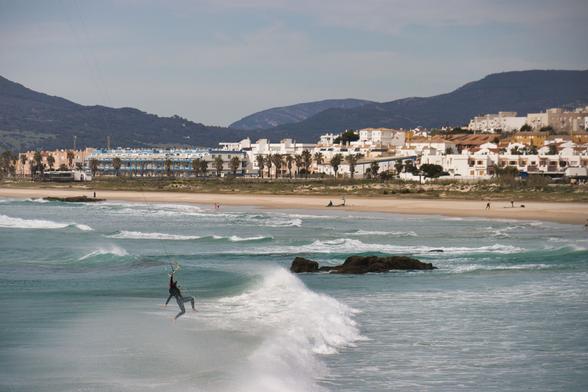 un uomo che pratica kite surf, sospeso a mezz'aria; sullo sfondo la città di Tarifa in Andalusia.