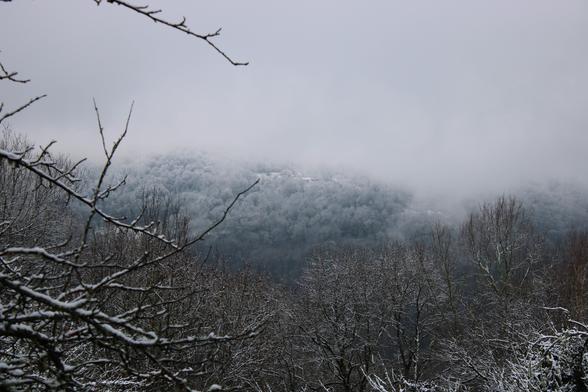 Paysage du Couserans par temps gris - un ciel gris uniforme, des traces de neiges au loin dans la brume neigeuse on devine deux maisons