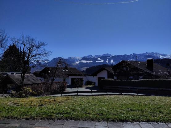 the image directly taken from a terrace in a small village shows a nice view towards the alps - nice weather and snowy mountains along w/ conifer forest