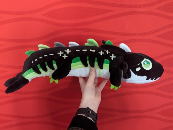 A photo of the profile of the longboi plush (an about 50cm long black and green dragon).