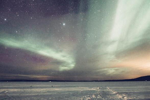 Un lac gelé couvert de neige en bas, et au dessus, jusqu'à l'horizon, le ciel rempli d'étoiles où se dessinent les traînées vertes d'aurore boréales