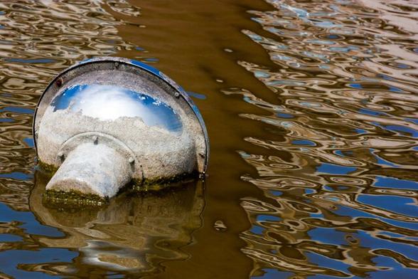 The lamp is now left in the middle. You can clearly see that it is completely rusted. Only the top part is shiny, in which the blue sky with clouds is reflected. It is windy so the water is rippled in the colors: dark brown, yellow and bright blue. A dark brown vertical wide stripe along the lamp comes from a work of art in the pond.