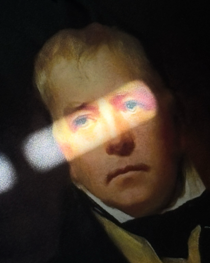 A cushion featuring a portrait of Sir Walter Scott has a shaft of light across the eyes on the portrait.