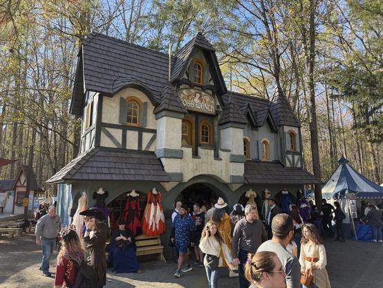 A medieval-style shop at a Renaissance fair, selling colorful dresses. People in costumes walk by, enjoying the lively atmosphere.
