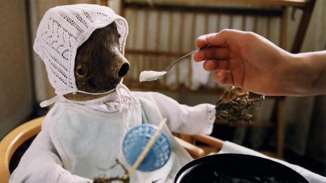 Otesánek is in a high chair as his mother tries to feed him. A scene from Jan Švankmajer's movie adaptation of the fairy tale.