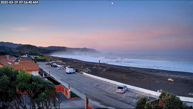 An early-morning view of Sharp Park Beach and Mori Point, with sea mist, a pink-purple sky, and a waning gibbous moon.