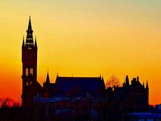 A Gothic university tower and surrounding buildings silhouetted against an orange and golden sunset.