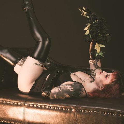 Rothaarige Frau in Dessous liegt auf Chaiselongue mit schwarzen Rosen in der Hand.