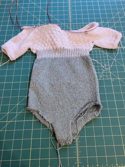 A small baby onsie. The bottom is plain, in a sage green color. The top is offwhite, short sleeves, with a cute bubble stitch pattern.