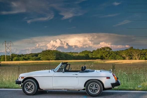 My 1980 MGB Roadster parked on the side of a rural road in front of a field and dramatic sky.