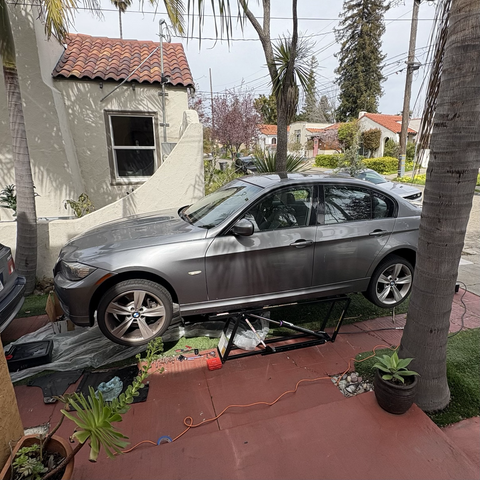 My gray 2009 BMW 335i sedan, raised on a QuickJack portable lift on my driveway, with a plastic tarp on the ground underneath to catch any runoff as I drain the transmission fluid.