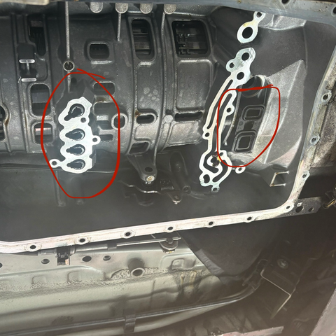 A view up into the ZF 6HP21 six-speed automatic transmission of my 2009 BMW 335i, with the oil pan and Mechatronic (valve body) unit removed. Towards the left, in about the middle of the transmission, four black plastic tubes are coming down through the housing, and to the right, at the front of the transmission, is a rectangular black plastic piece with two smaller rectangular oil passages. These common wear items that I replaced are circled in red.