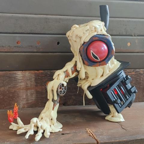 A miniature of a candle wax golem stacked on top of a leaning cast iron stove. The golem has a large, rusted hex nut with a red eye in the middle. Extending from its body and to the ground is an arm of wax and metal parts.  Wax fingers spread across the ground and there are flames on two fingertips. A red glow is emitted from the belly of the stove and some wax is spilling out.