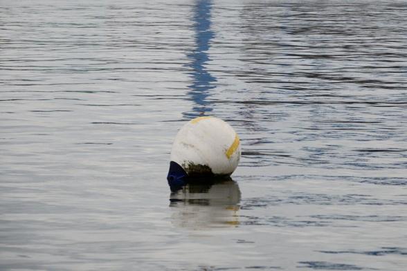 A buoy on the water with a line of blue reflection in the background