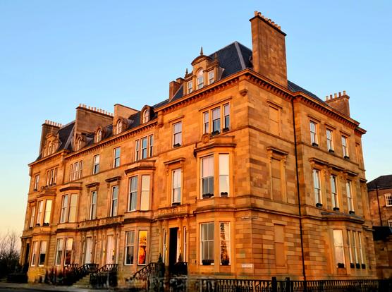 Blonde sandstone Victorian townhouses glowing orange in the reflected light of a sunset.