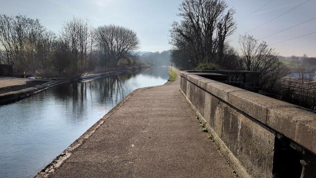 A view from the top of the Aqueduct of the canal stretching out into the distance. Trees can be seen either side and their reflections in the canal below. Above blue sky with whisky clouds.